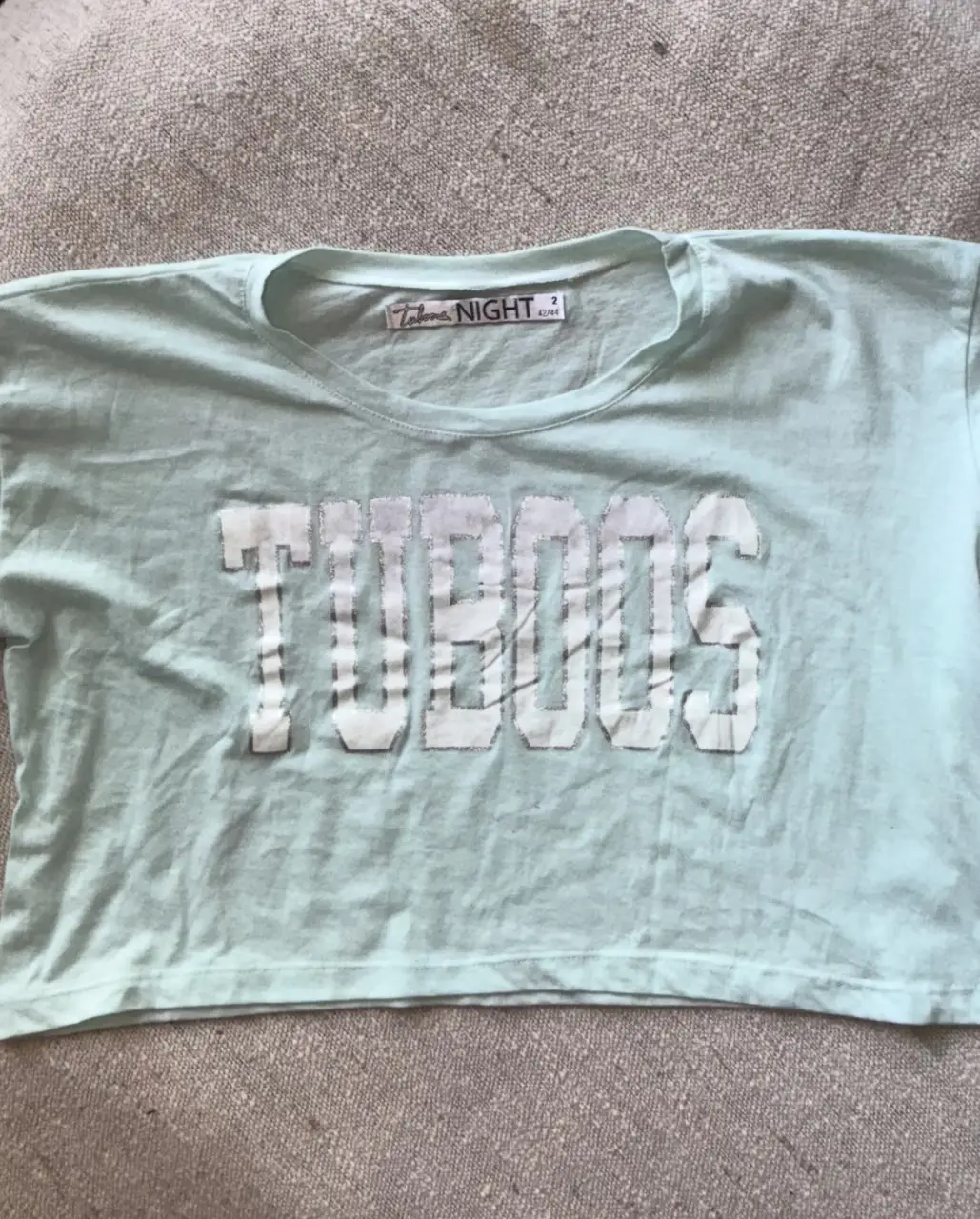 Remera crop de mujer celeste con estampado "TUBOOS NIGHT". Tiene mangas cortas con detalles de rayas blancas. Ideal para un look casual y moderno.