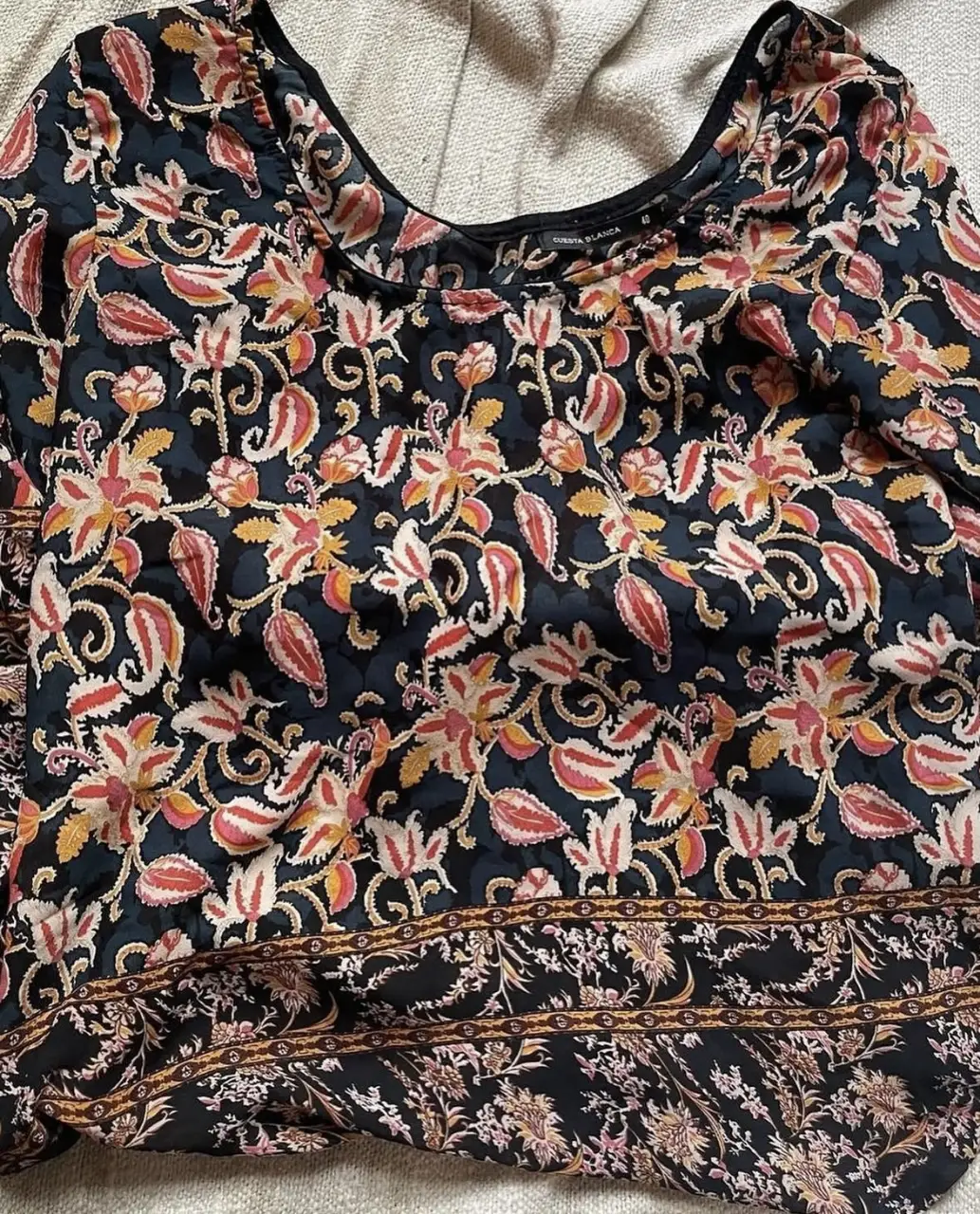 Blusa estampada con diseño floral en tonos rosa, amarillo y rojo sobre fondo negro. Cuello redondo y mangas 3/4. Ideal para un look casual y femenino.