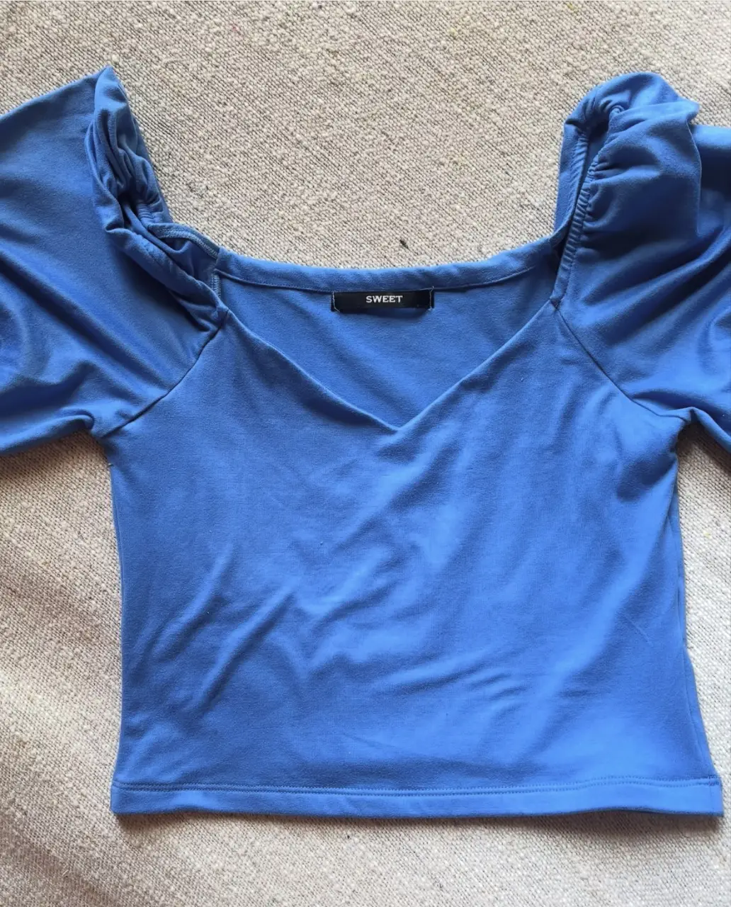 Top azul con mangas abullonadas, escote en V y detalle de la marca "SWEET". Ideal para un look moderno y femenino.