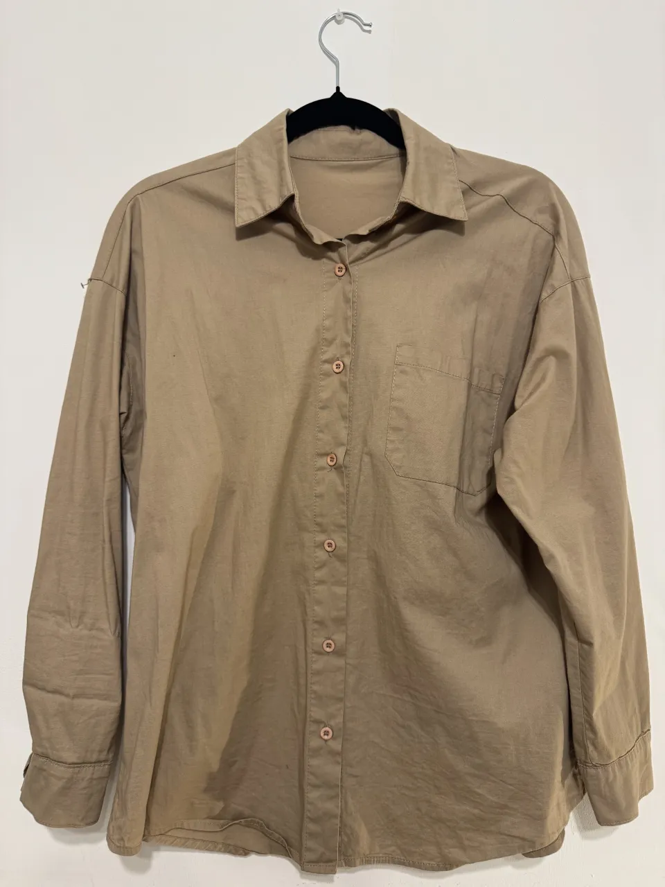 Camisa de manga larga color beige con botones al frente y bolsillo en el pecho.