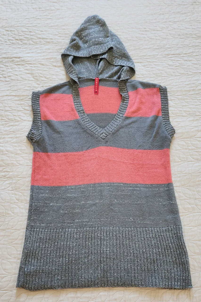 Buzo con capucha, sin mangas, de tejido a rayas grises y rosas. Posee cuello en V.
