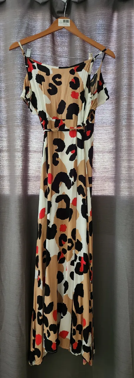 Vestido largo estampado de leopardo en tonos beige, blanco, negro y rojo. Posee tiras finas, cuello cruzado y lazo para atar en la cintura. Tiene un corte con tajos laterales.