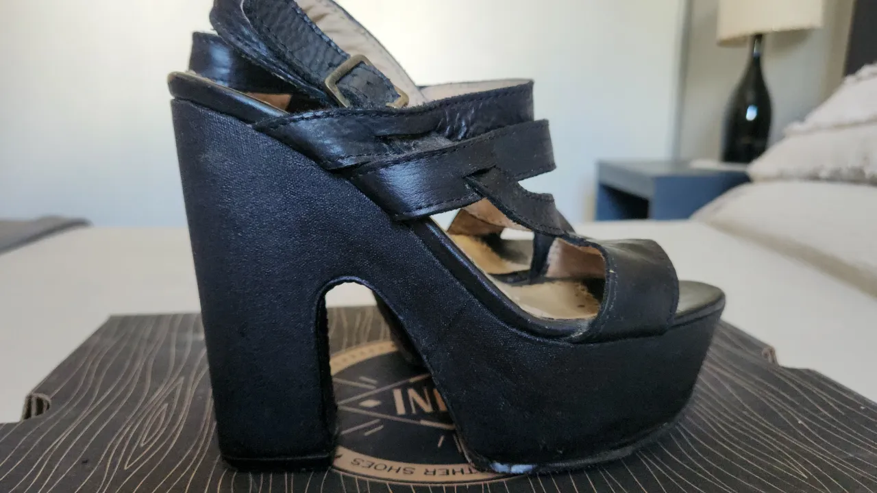 Sandalias negras con plataforma y taco grueso. Tienen tiras finas que cruzan sobre el empeine y una tira en el tobillo con hebilla.