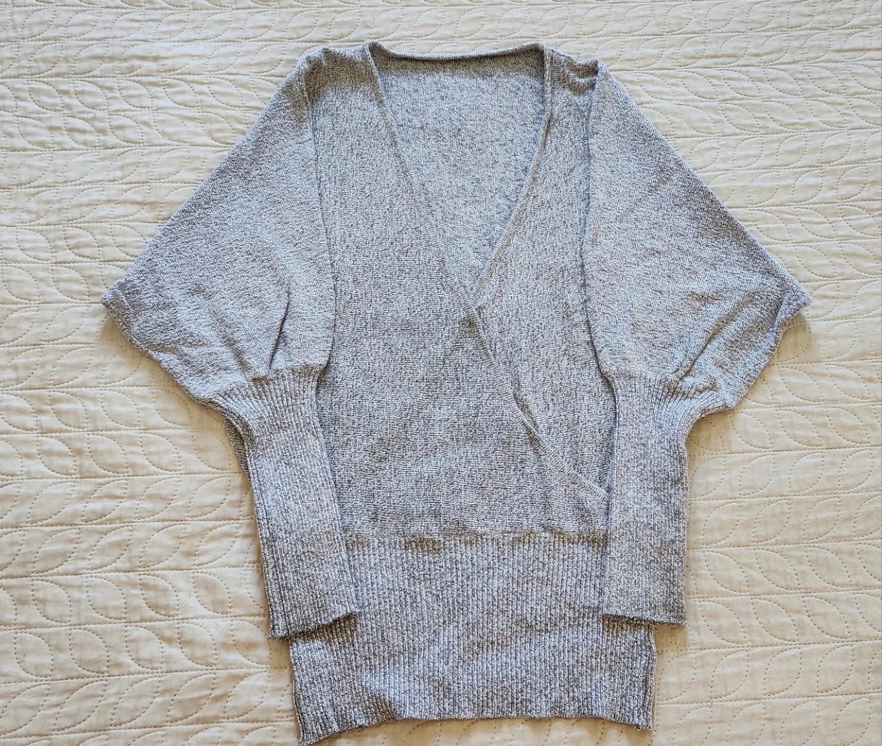 Sweater gris jaspeado con escote cruzado en V y mangas amplias tipo murciélago. Puños y cintura de ribb.