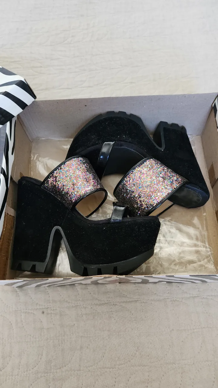 Sandalias negras con plataforma y taco grueso. Tienen tiras con glitter multicolor en la parte delantera y una tira fina negra sobre el empeine. La suela es de goma con un diseño marcado.
