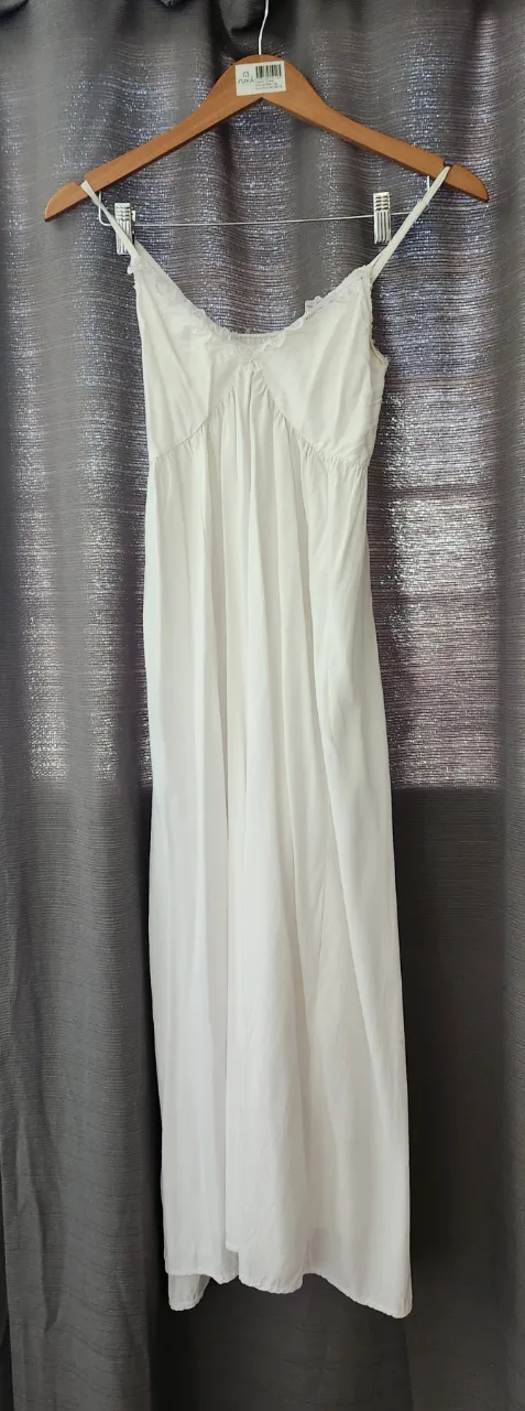 vestido blanco largo con tirantes finos y detalles de encaje en el escote. Posee tajos laterales.