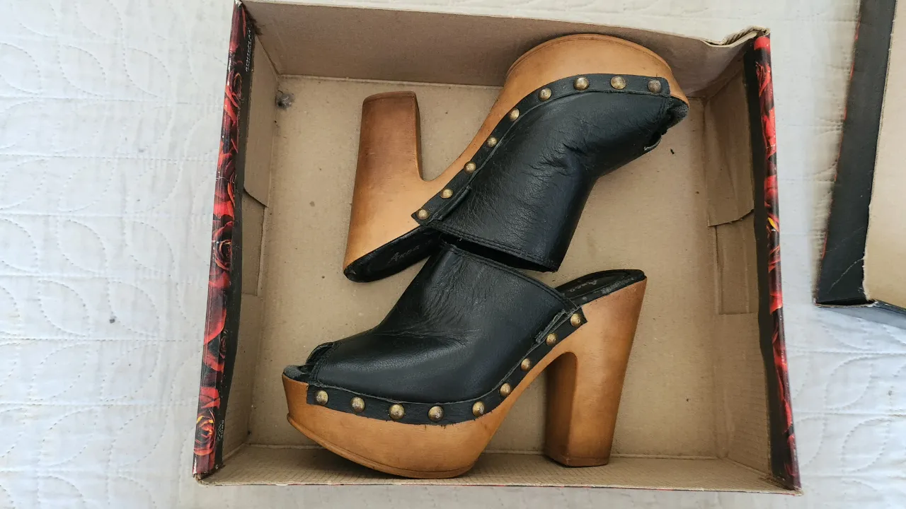Zuecos negros de cuero con taco de madera y tachas metálicas. La punta es abierta.