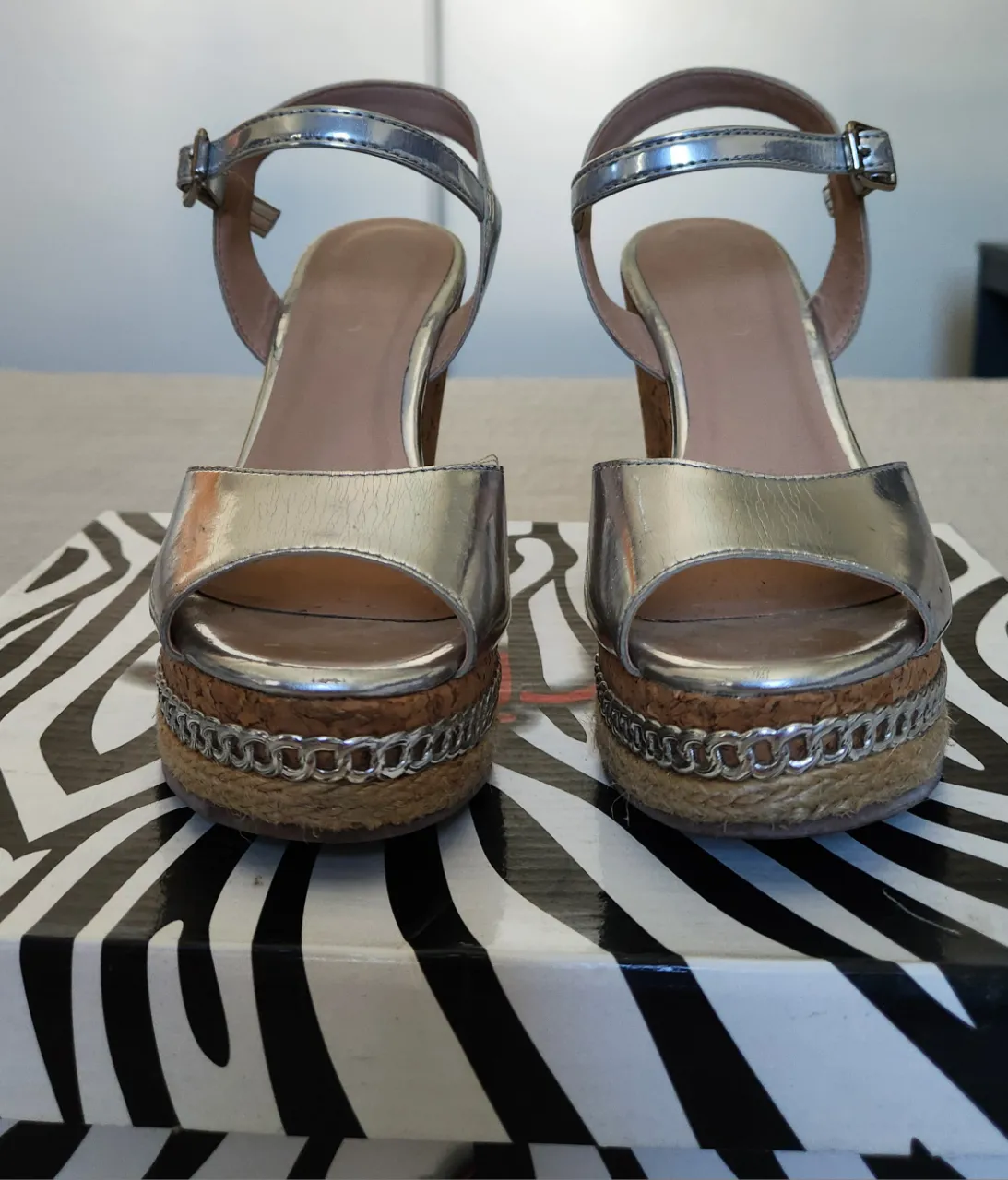 Sandalias de plataforma con taco cuña. Tienen tiras plateadas y detalle de cadena metálica en la base de la plataforma. Cierre con hebilla.