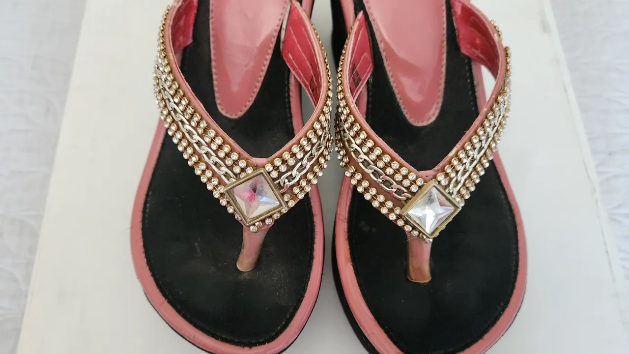 Ojotas con plataforma y tiras adornadas con cadenas y strass. La base es negra y las tiras son color rosa metalizado.