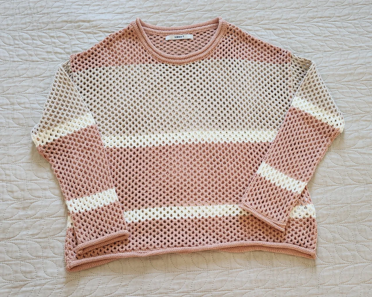 Sweater de tejido de red a rayas horizontales en tonos rosa pálido y blanco. Cuello redondo y mangas largas.