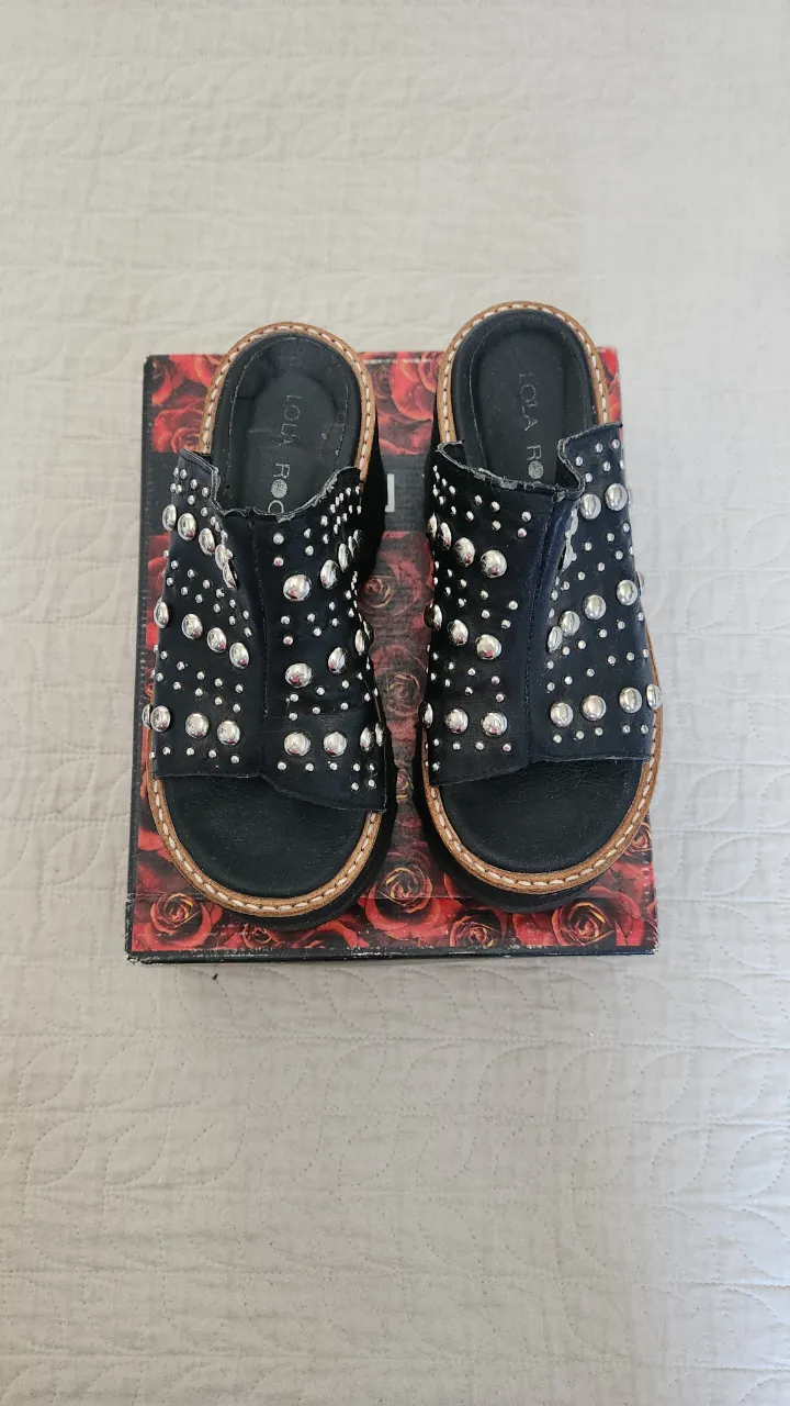 Sandalias negras con plataforma alta, tiras adornadas con tachas plateadas y suela gruesa con relieve.