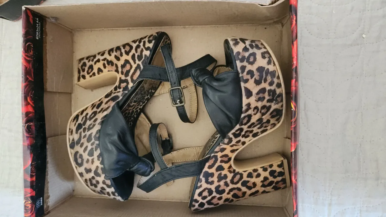 Sandalias de plataforma con taco alto y estampa de leopardo. Tienen tiras negras con hebilla y un moño negro en la punta.