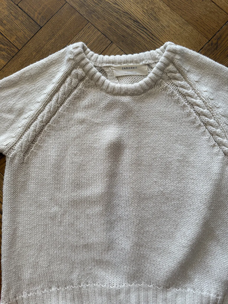 Sweater tejido color crudo con detalles de trenzas en los hombros, mangas 3/4 y espalda abierta.