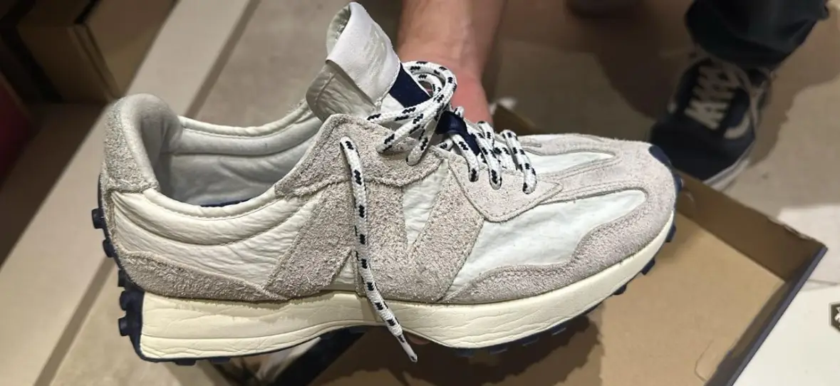 Zapatillas New Balance 327 en tonos neutros, con detalles en azul marino y cordones a contraste. Ideales para un look casual y moderno.