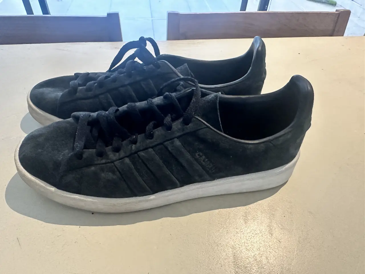 Zapatillas Adidas Campus negras de gamuza, con suela blanca. Un clásico atemporal para un look casual y cómodo.