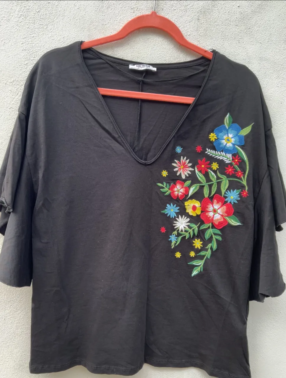 Remera negra con escote en V y bordado de flores de colores en el frente. Mangas cortas con volados.