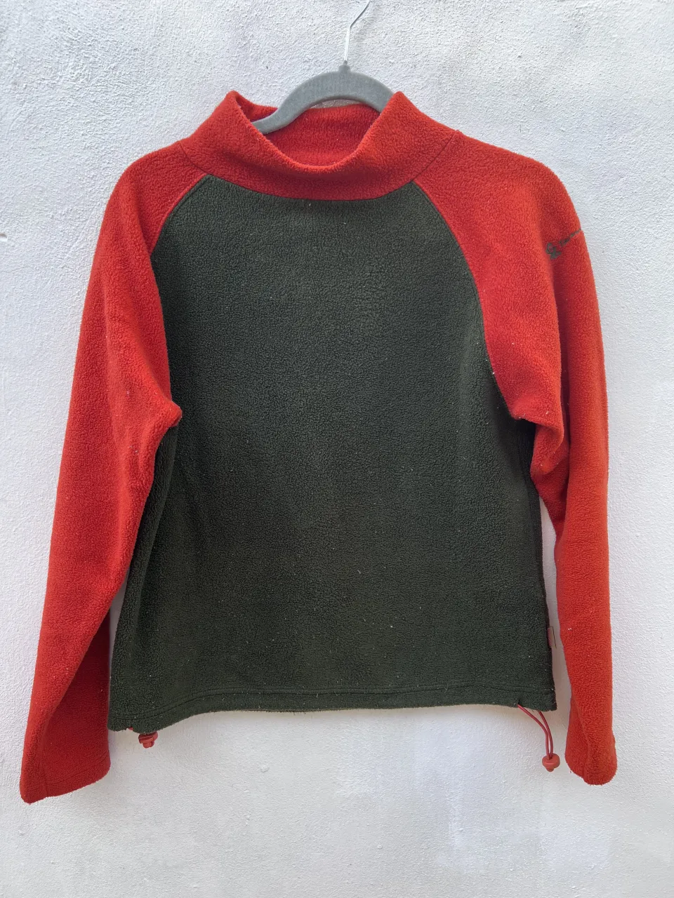 Buzo de polar con cuello alto. Posee cordones ajustables en la parte inferior.