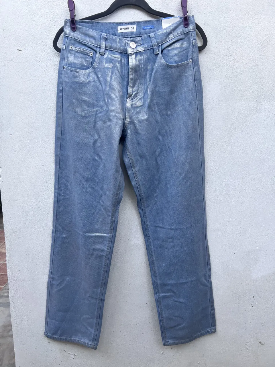 Jeans de tiro recto con lavado celeste y detalles plateados desgastados. Cierre de botón y bolsillos frontales y traseros.