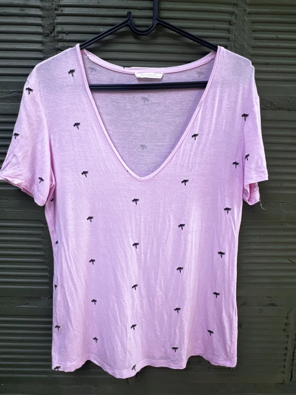 Remera manga corta de color rosa pálido con estampa de palmeras negras. Escote en V pronunciado.