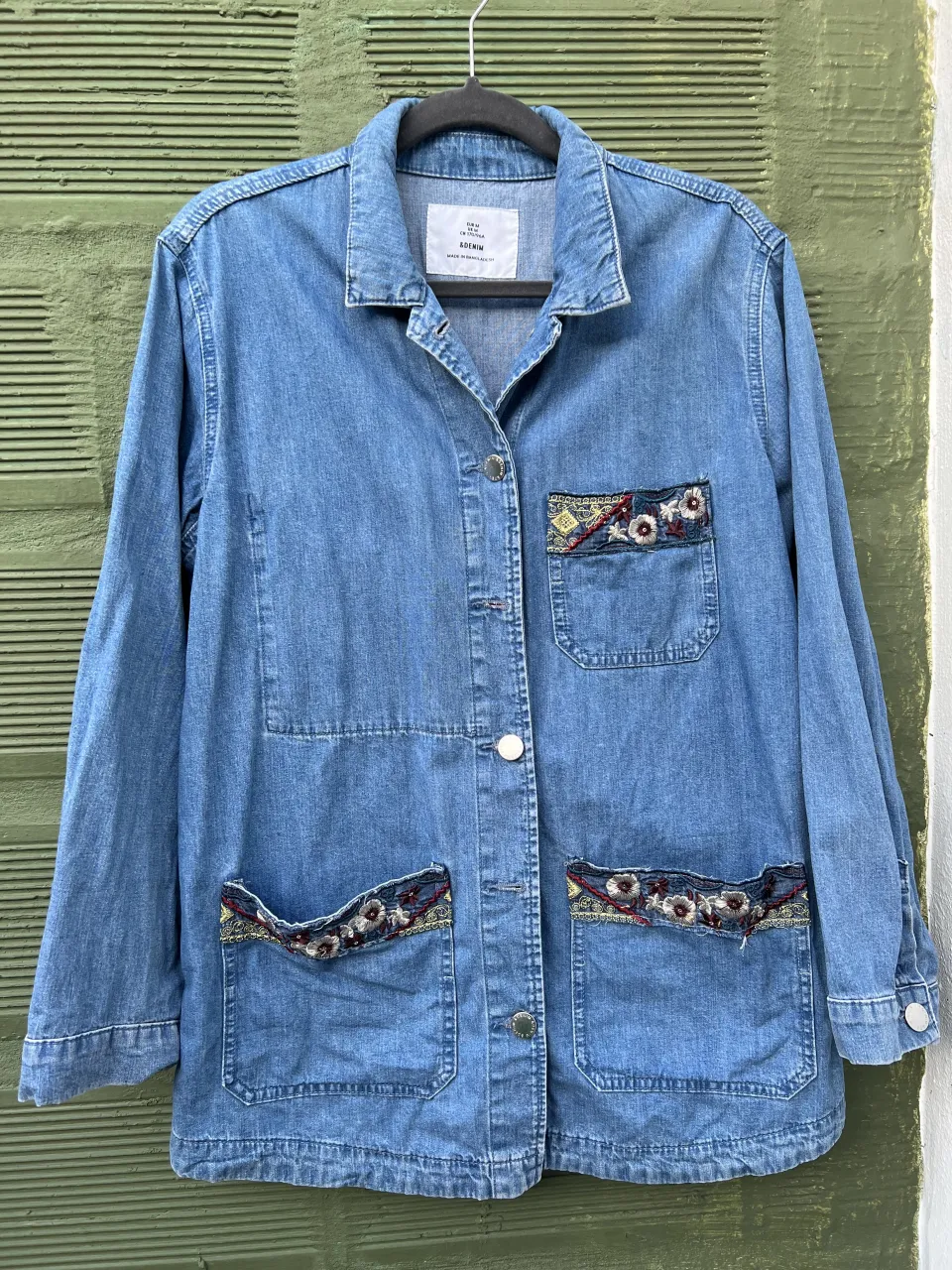 Campera de jean azul con bolsillos delanteros y detalles bordados en los mismos. Cierre de botones al frente. Oxford