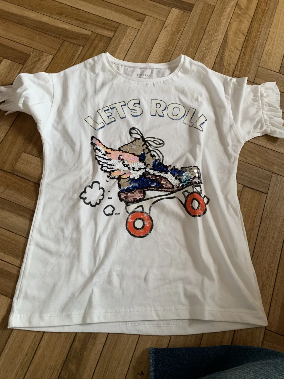 Remera blanca con estampa de patines y la frase "lets roll". La estampa tiene lentejuelas.