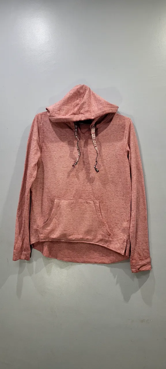 Buzo con capucha de color salmón jaspeado. Posee bolsillo canguro al frente y cordones en la capucha.