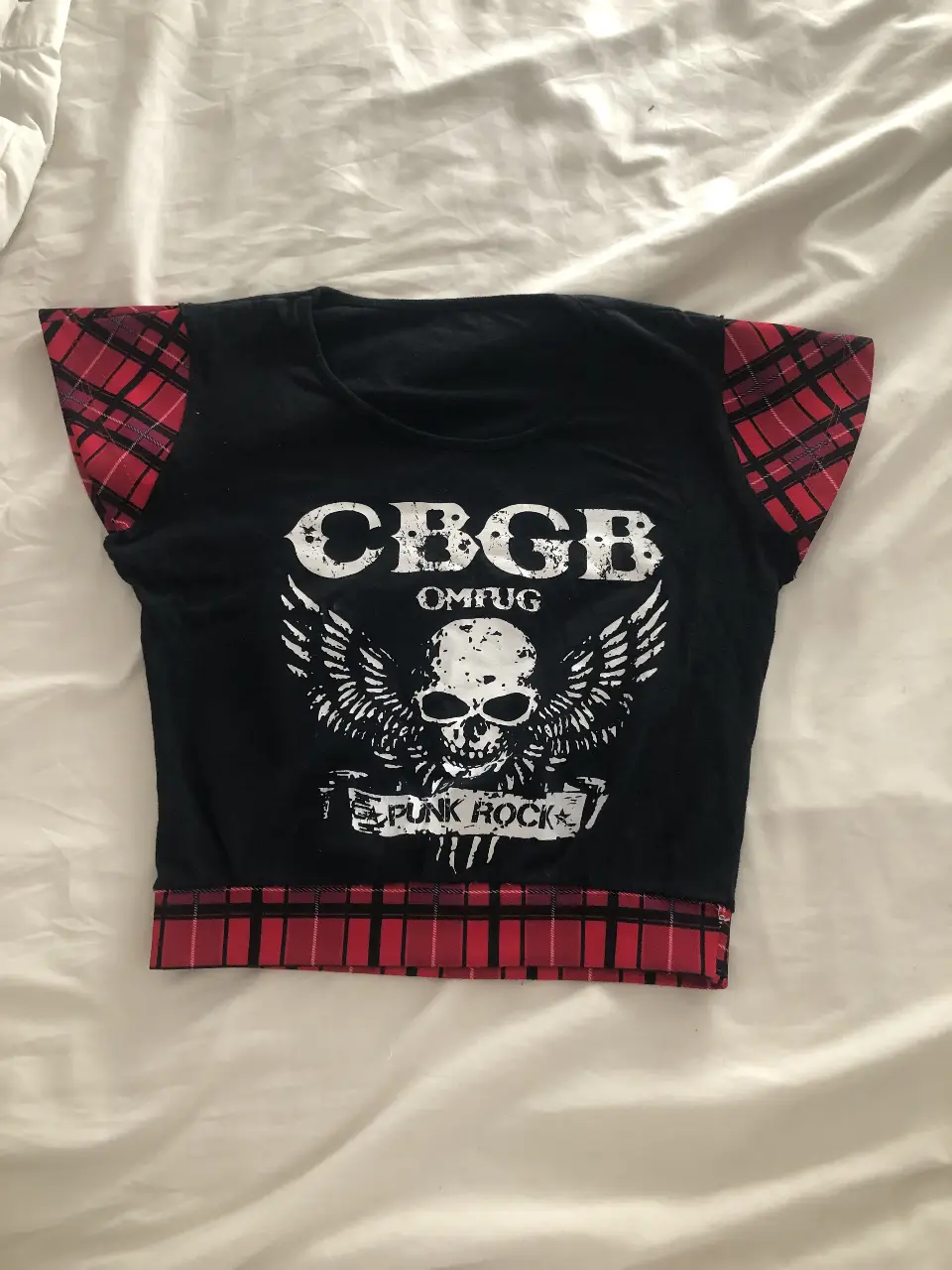 Remera crop top intervenida de mujer con estampado CBGB Punk Rock. Mangas y borde inferior con tela a cuadros rojos y negros. Ideal para un look rocker y casual.