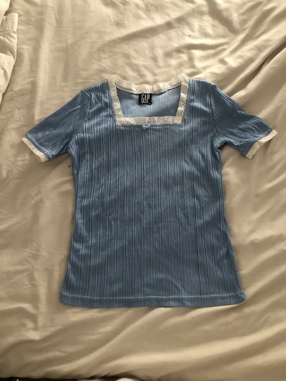 Remera de manga corta azul claro con detalles de encaje blanco en el cuello cuadrado y en las mangas. Estilo Y2K, ideal para un look retro y femenino.