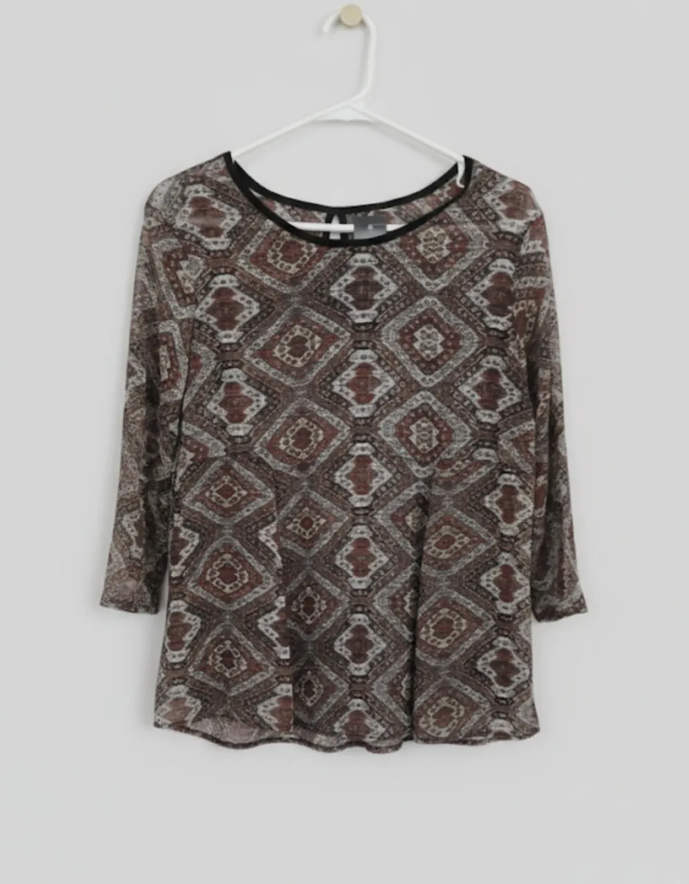 Blusa estampada con cuello redondo y mangas 3/4. Presenta un diseño geométrico en tonos tierra y azul.