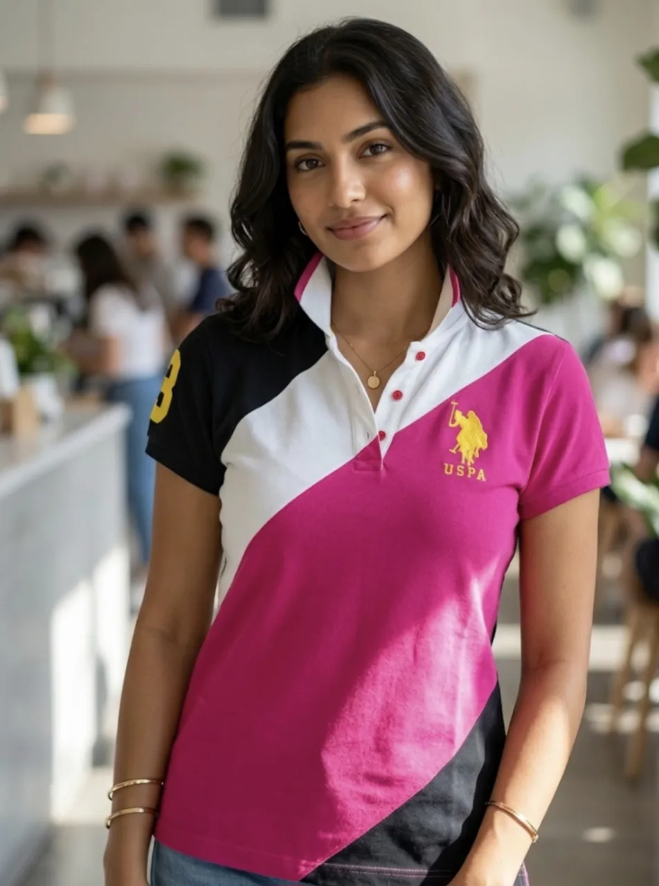 Remera polo de mujer con cuello y mangas cortas. Diseño de bloques de color en fucsia, blanco, negro y detalles en amarillo. Logo de la marca bordado en el frente y número grande en la manga.