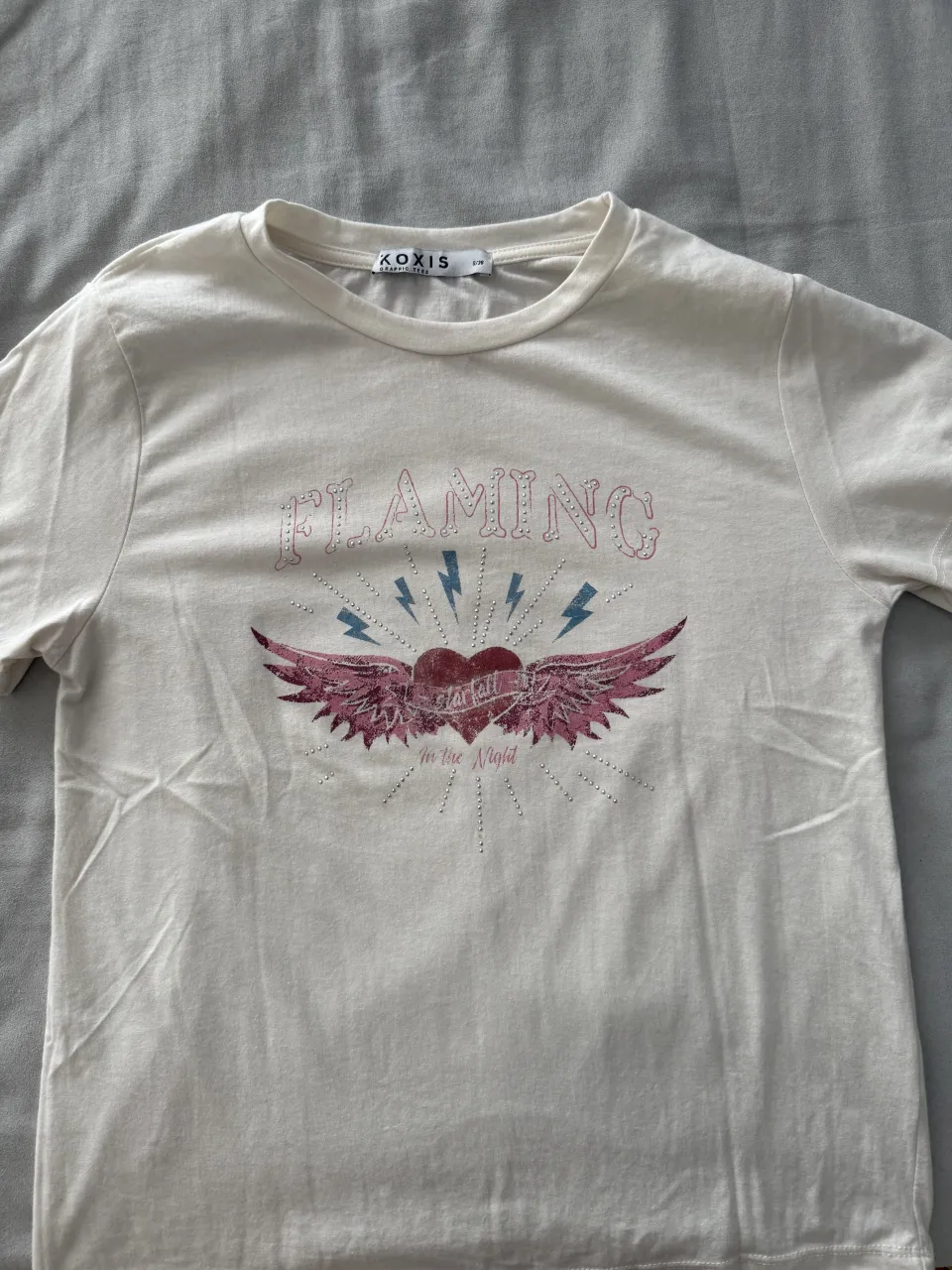 Remera blanca con estampa "Flaming" y un corazón alado. Ideal para un look casual y con onda.