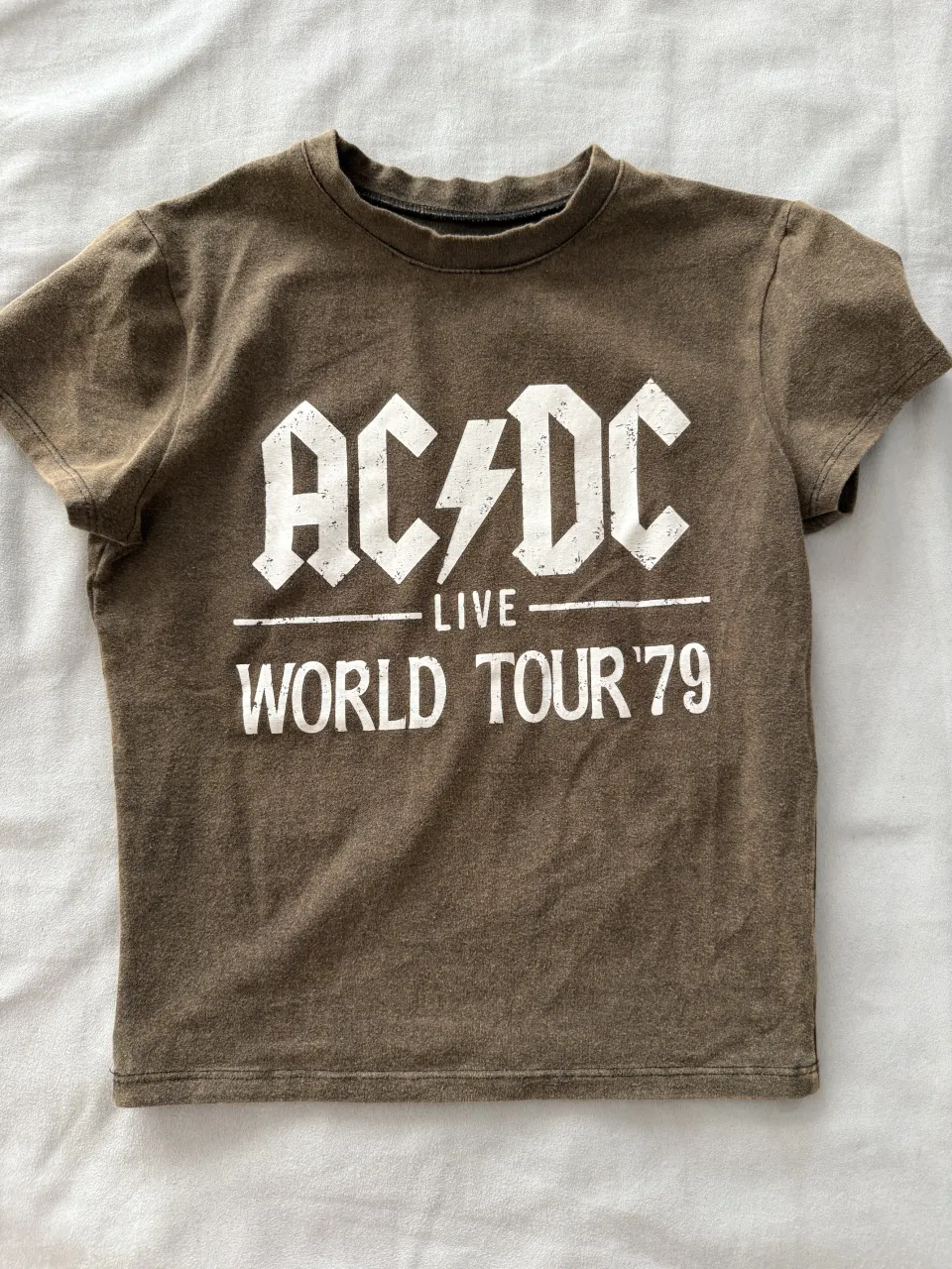 Remera de manga corta marrón con estampa "AC/DC LIVE WORLD TOUR '79" en blanco. Ideal para fans de la banda y para un look casual.