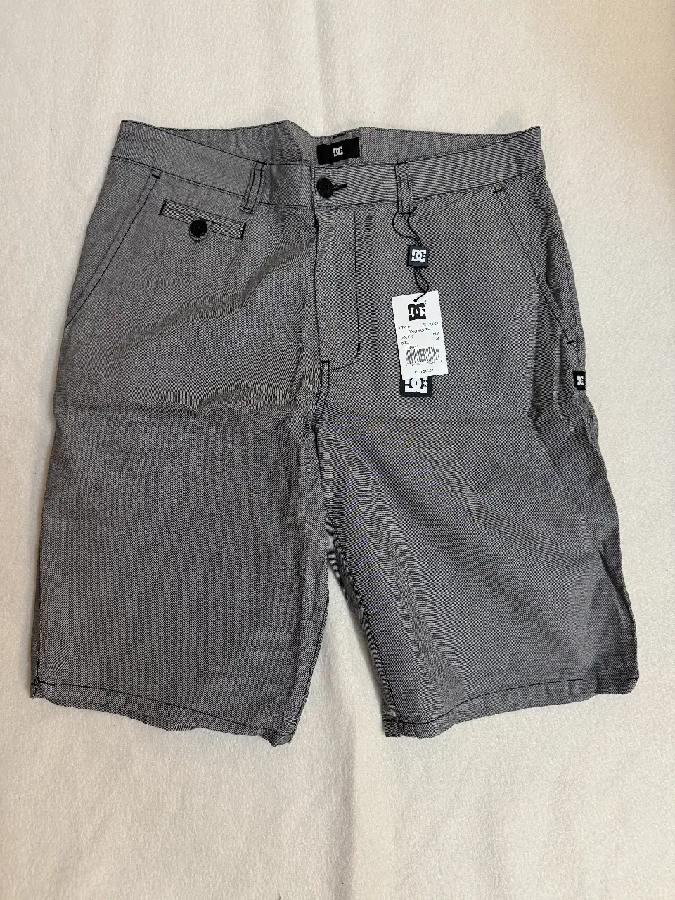 Short de hombre DC, color gris con diseño de líneas. Ideal para un look casual y cómodo. Cuenta con bolsillos y etiqueta de la marca. Talle 30 Estados Unidos.