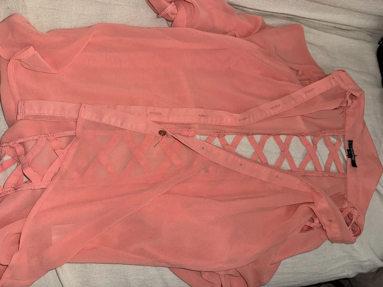 Camisa importada color coral con botones al frente y detalle de tiras cruzadas en la espalda. Mangas largas con puños abotonados.