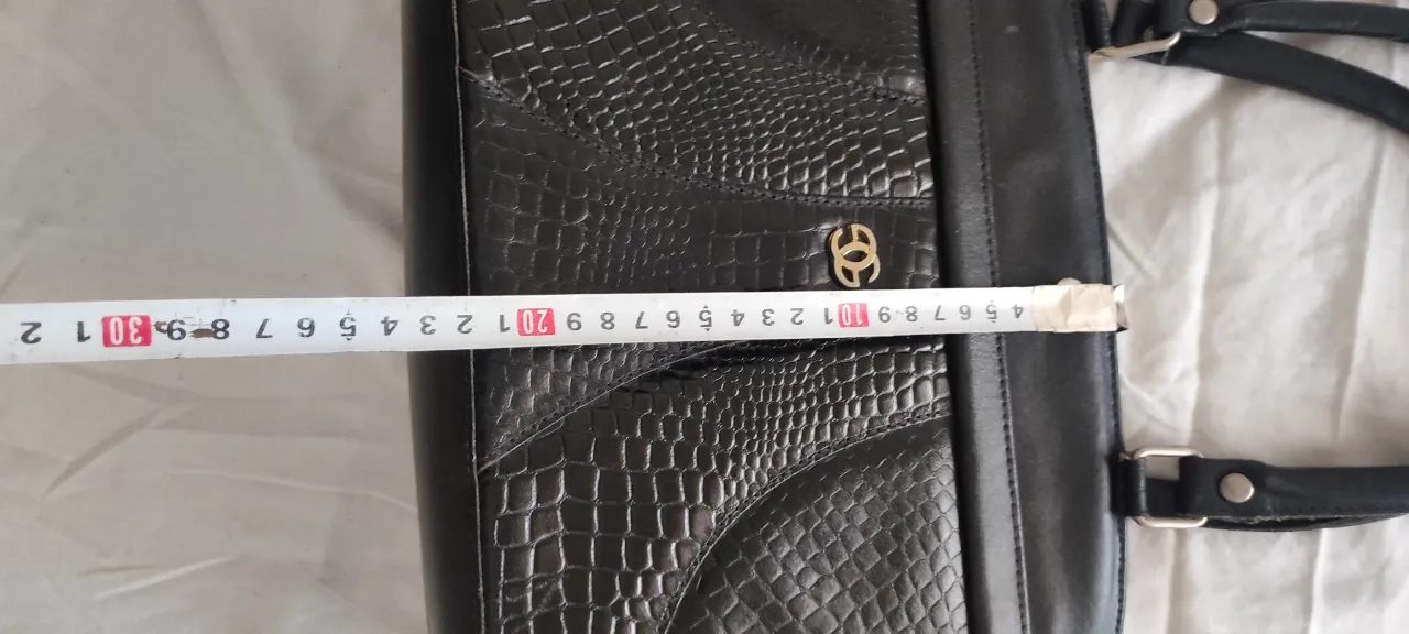 Cartera negra de cuero sintético con textura de cocodrilo y detalles en cuero liso. Posee un logo dorado en el frente y múltiples compartimentos internos con cierre. Ideal para el día a día o para un look elegante.