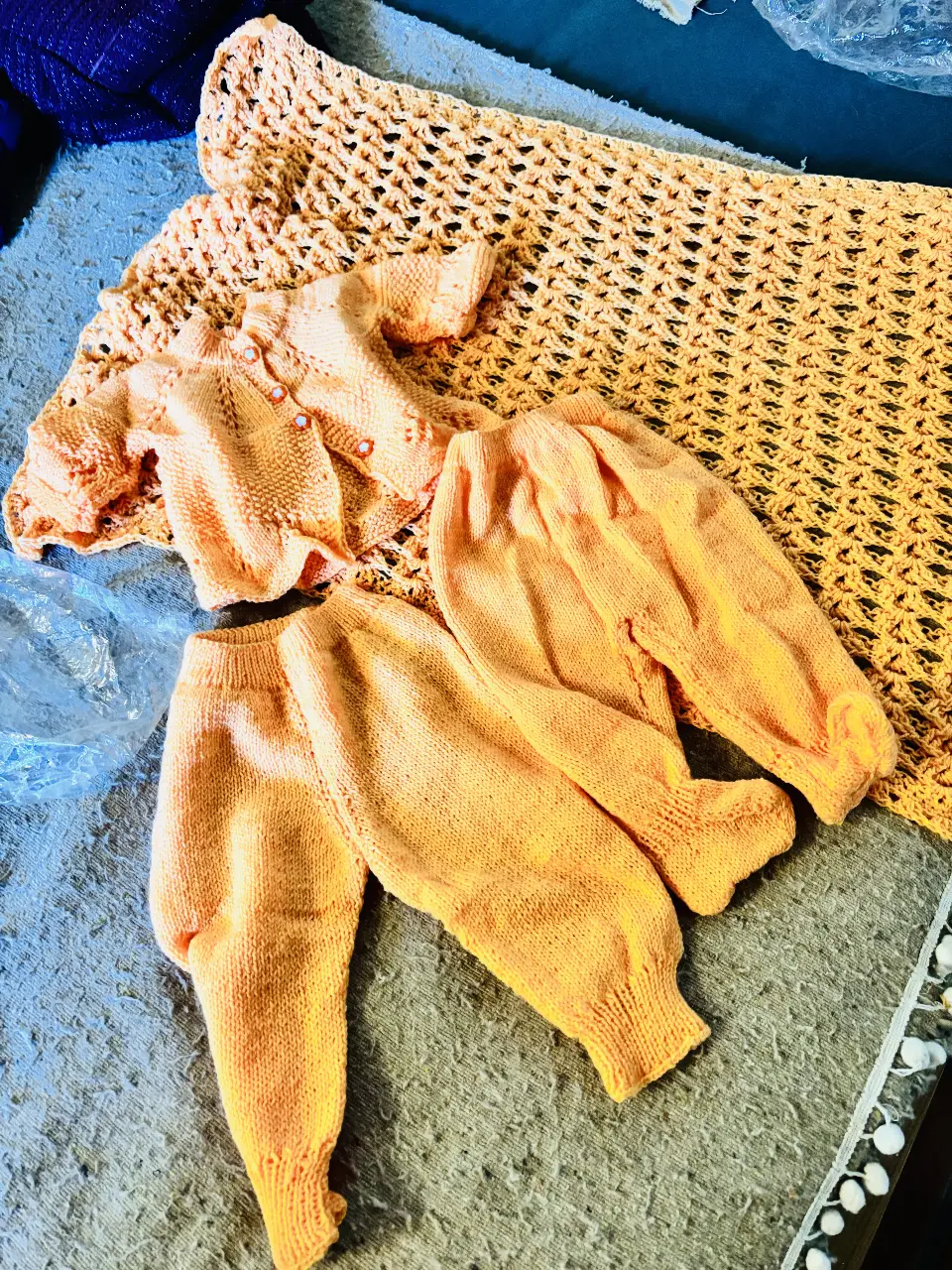 Conjunto de bebé tejido a mano en color naranja. Incluye un sweater con botones, un pantalón y una manta calada. Ideal para abrigar y vestir a tu bebé con estilo artesanal.