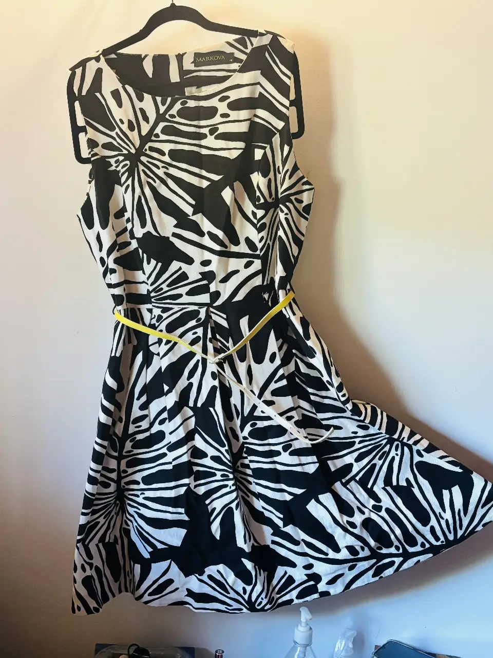 Vestido midi de la marca Markova, con estampado de hojas en blanco y negro. Tiene un cinturón amarillo para ajustar la cintura. Ideal para una ocasión especial o para un look elegante.