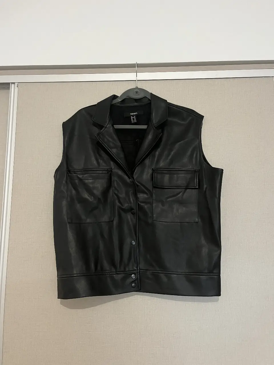 Chaleco de cuero sintético negro de Forever 21, con cuello solapa y dos bolsillos delanteros. Talle M.