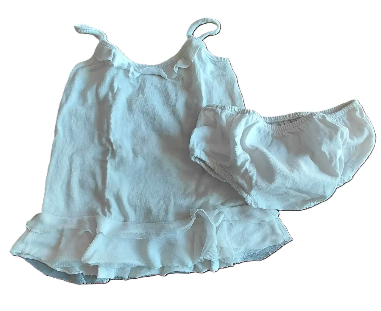 Conjunto de dos piezas blanco, compuesto por una vestido con volados en el cuello y terminación con volados de tul en la parte inferior, y un bombacha cubre pañal  con elástico en la cintura y terminación con volados.