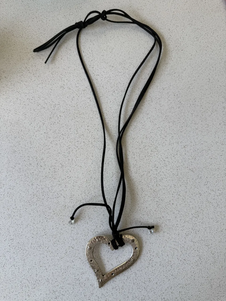 Collar con dije de corazón plateado y cordón negro ajustable. Ideal para un look casual o bohemio.