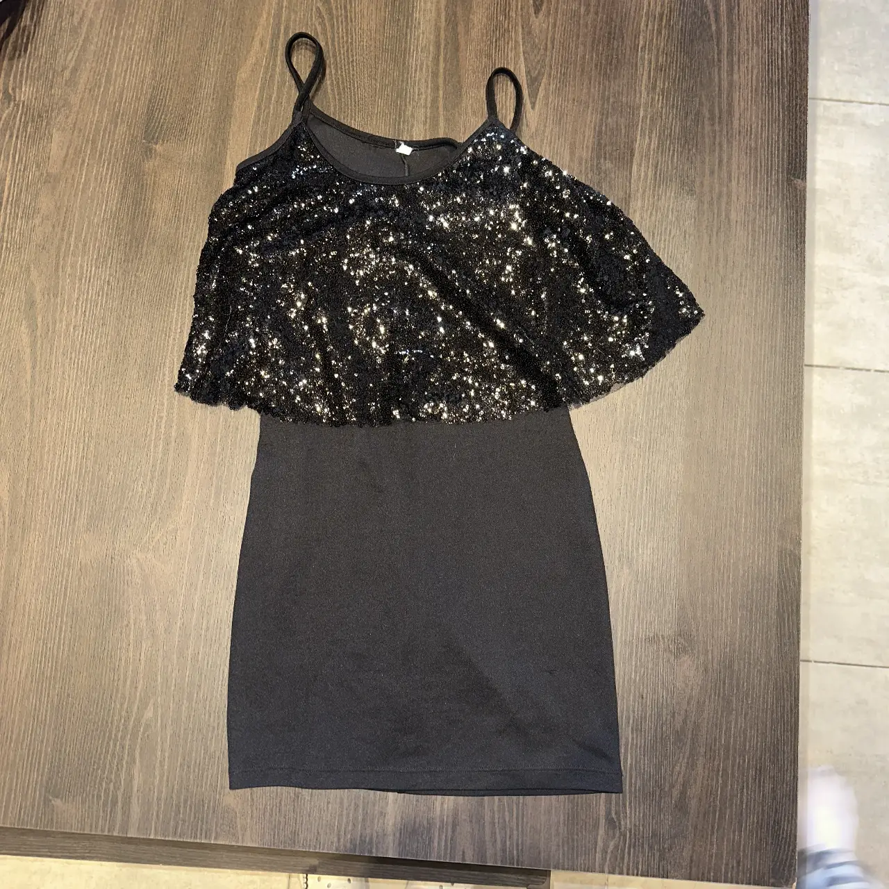 Vestido negro mini con detalle de lentejuelas en la parte superior, ideal para fiestas y eventos especiales. Un diseño moderno y elegante para lucir en cualquier ocasión.