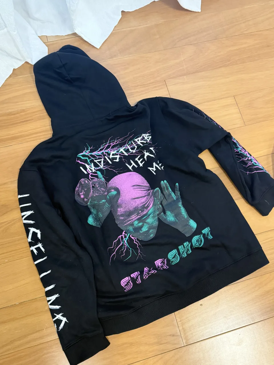 Buzo negro con capucha y estampa gráfica en el frente y mangas. La estampa incluye un rostro con una banda en la cabeza, manos y rayos de colores neón.