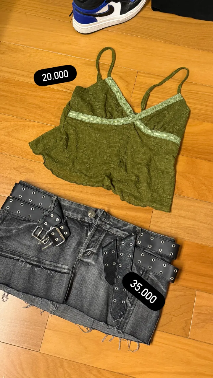 Remera verde con breteles finos y detalles de encaje en el escote. Pollera de jean gris con doble cinturón negro con tachas y roturas.