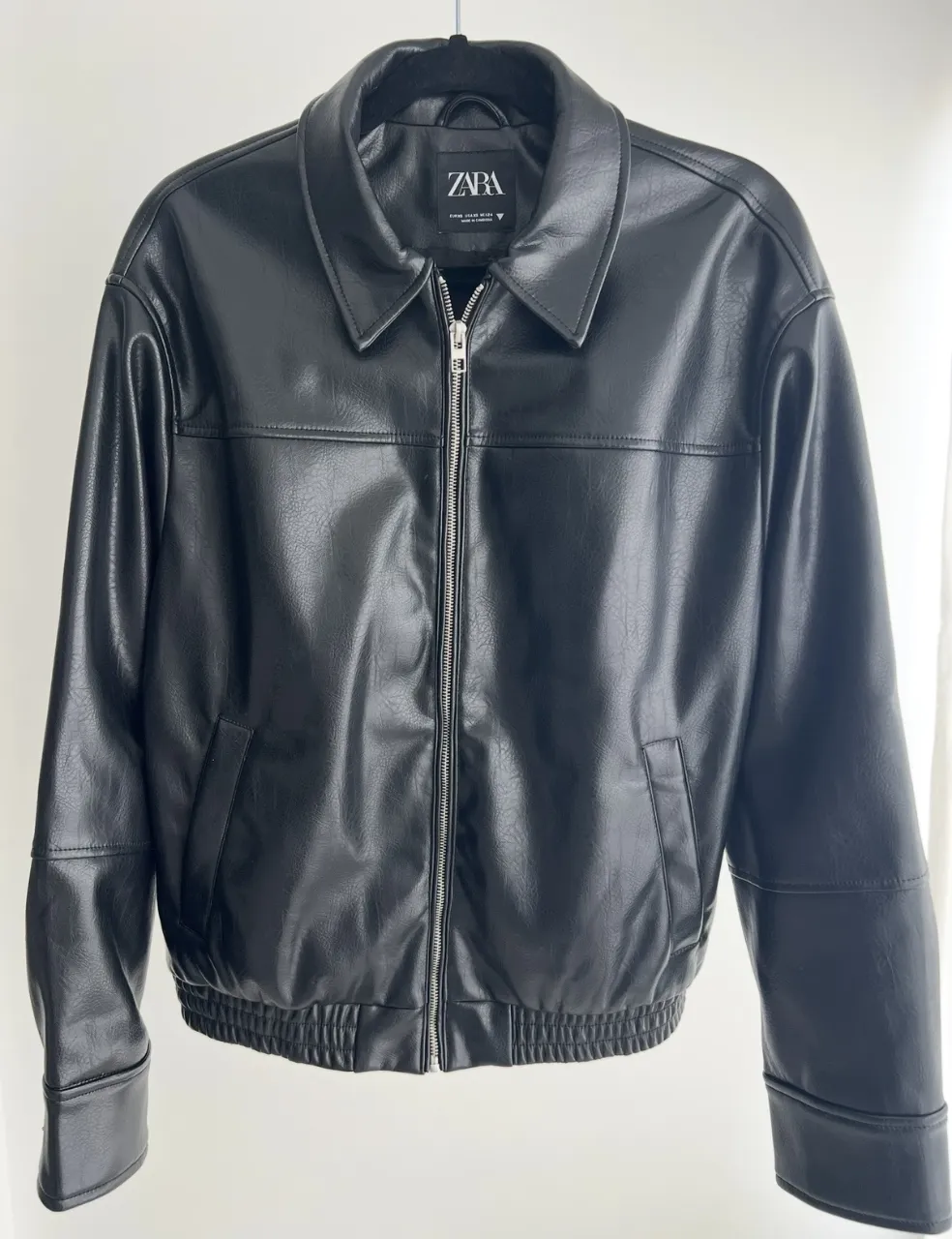 Campera de cuero sintético negra con cuello, cierre al frente y puños y cintura elastizados.