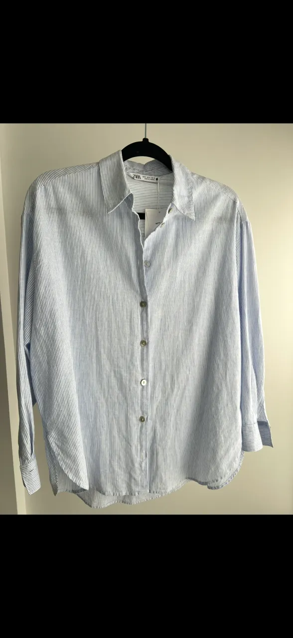 Camisa a rayas celestes y blancas, con botones al frente y cuello clásico.