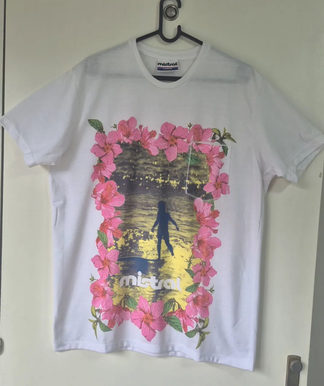 Remera blanca de manga corta con estampa de flores rosas y una persona surfeando. Ideal para un look casual de verano.