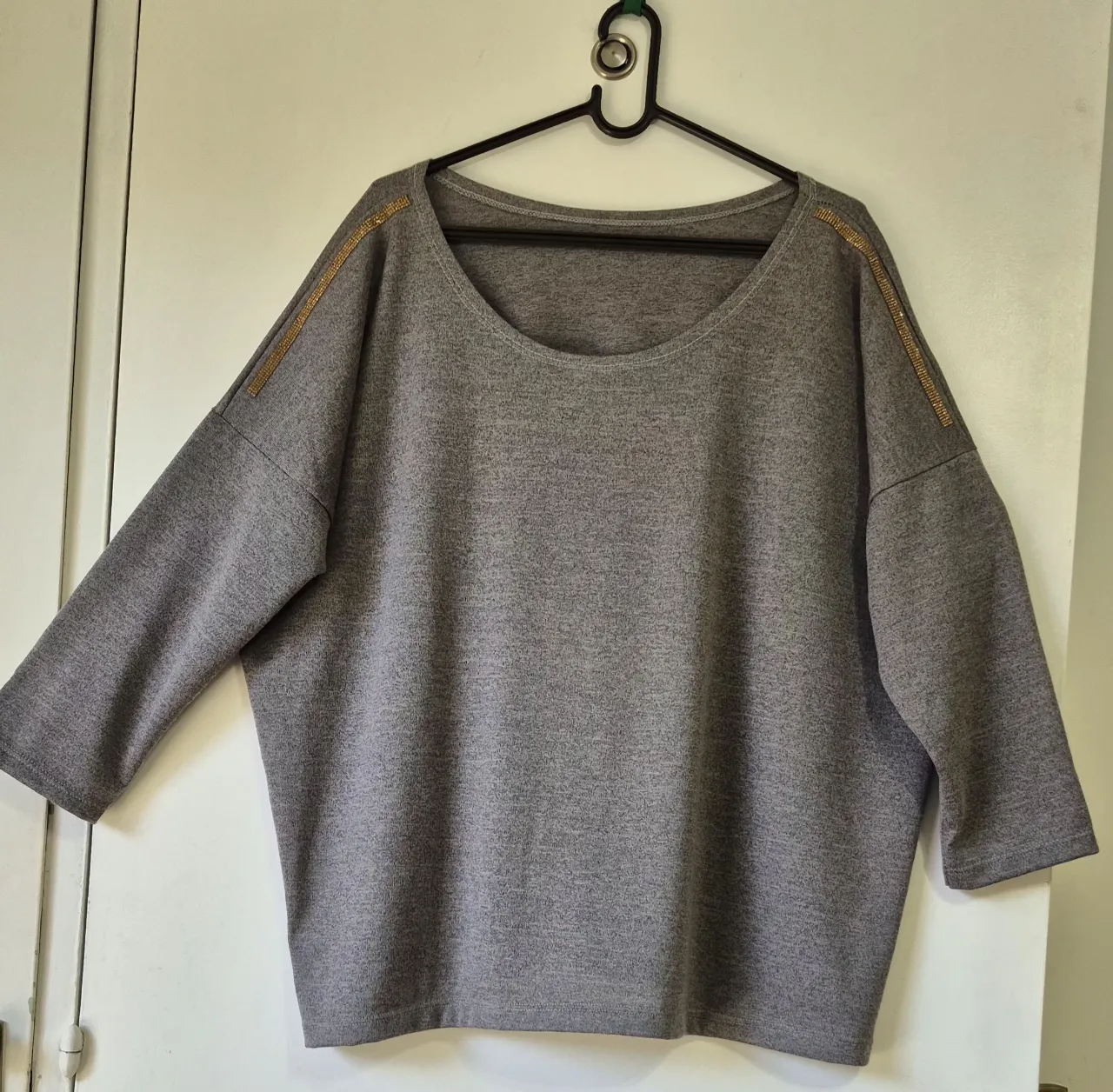 Remera gris melange de mangas 3/4, con detalles de strass dorado en los hombros. Es súper cómoda y canchera, ideal para el día a día.