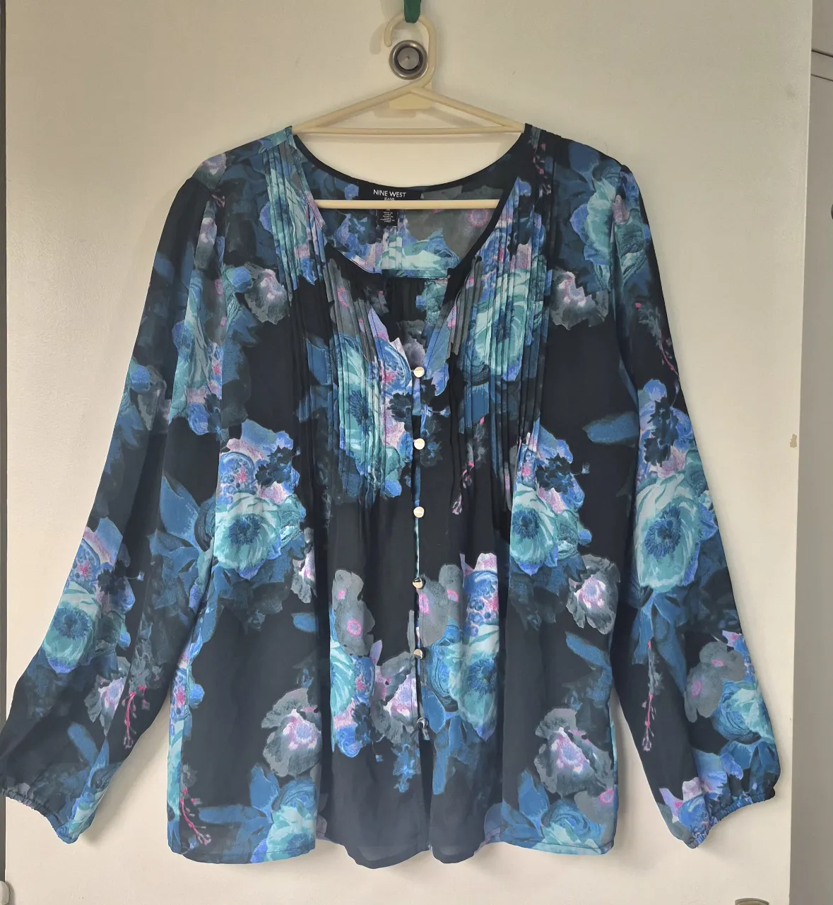 Blusa estampada con flores en tonos azules y rosas sobre fondo negro. Posee cuello en V con botones y mangas largas con puños. Ideal para un look elegante y femenino.