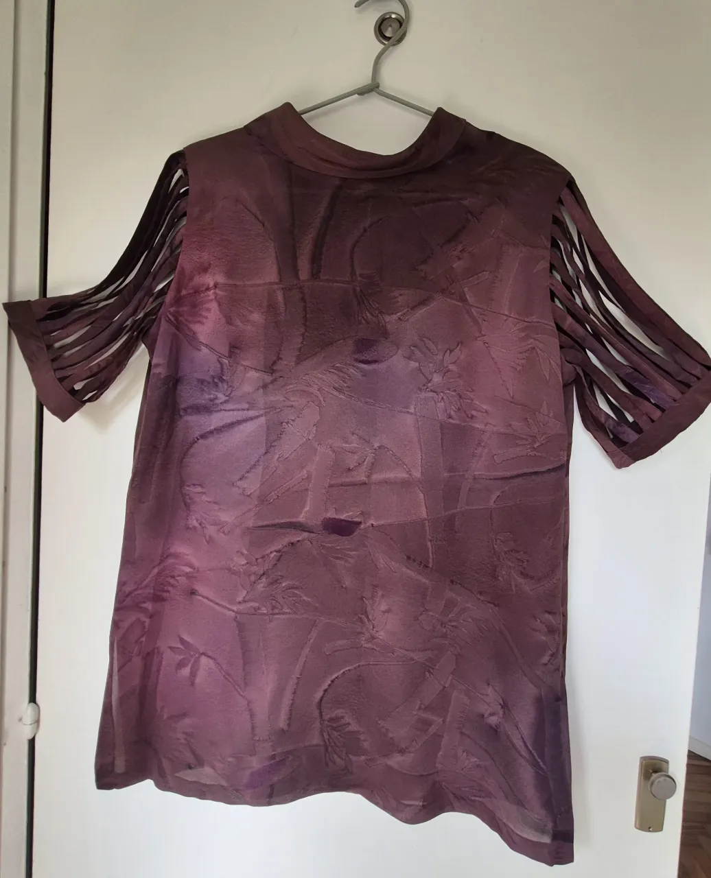 Blusa de viscosa con cuello mao y mangas cortas con tajos verticales. Posee un estampado floral abstracto en tonos morados y rosados.