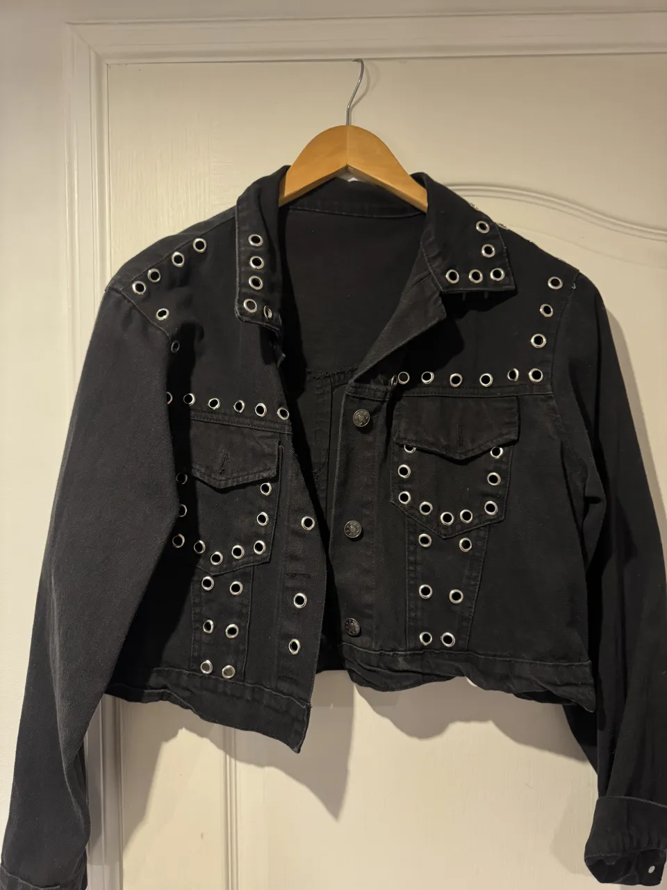 Campera de jean negra corta con tachas plateadas redondas en cuello, solapas, bolsillos y puños. Cierre de botones al frente.